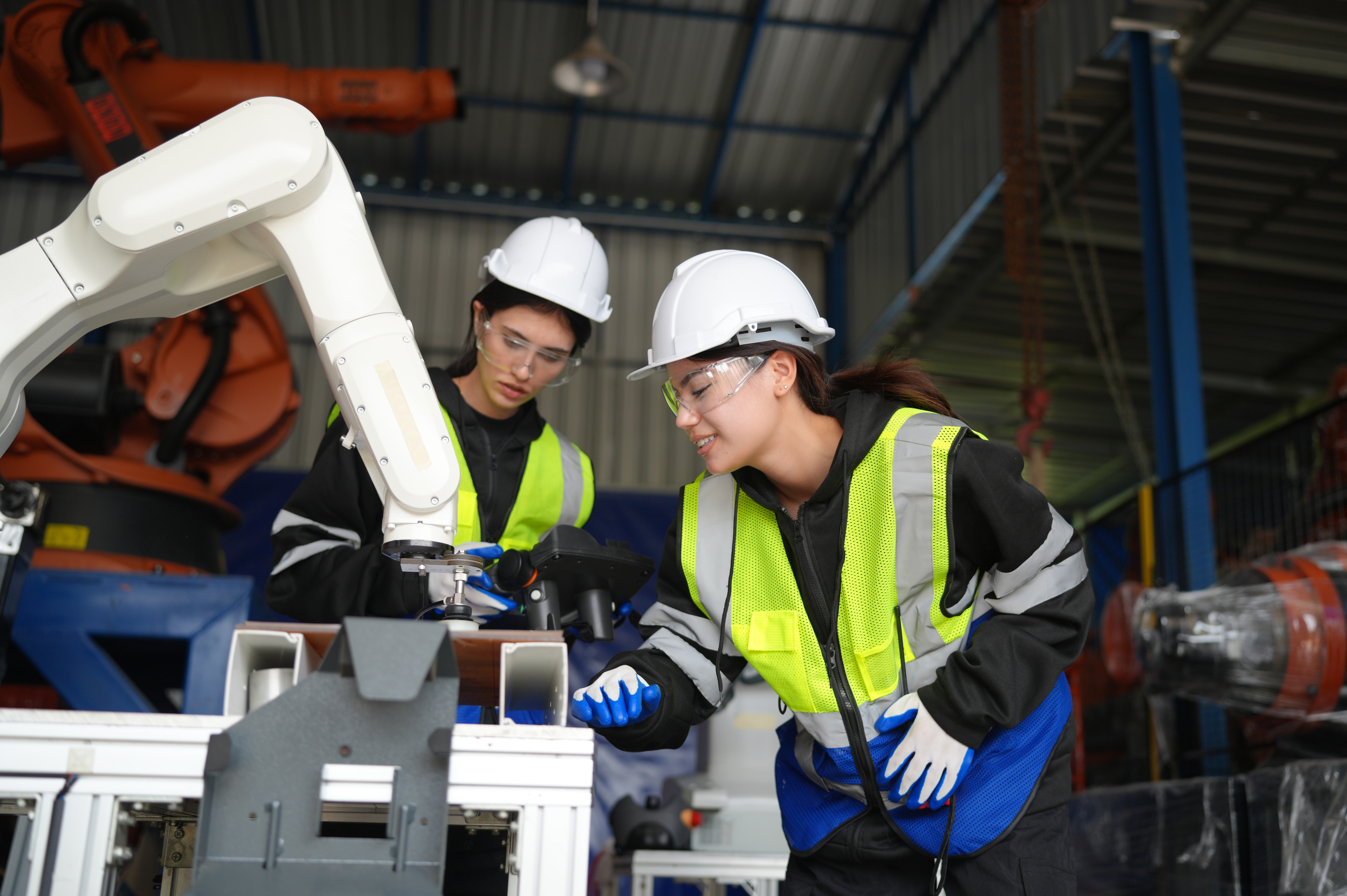 Two engineers working with a robotic arm on a factory floor